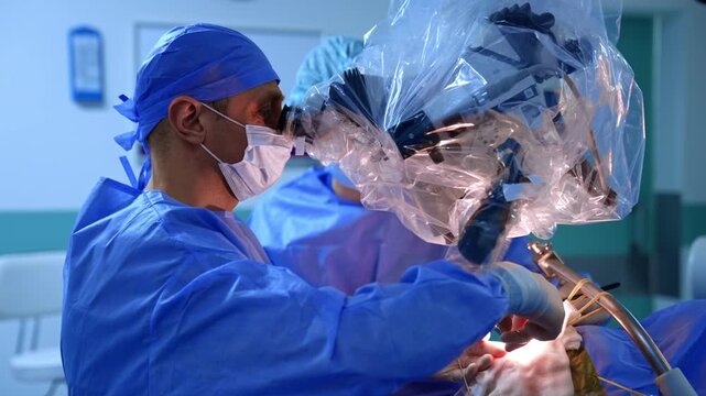 Professional neurosurgeon looks attentively to the microscope and carefully uses medical tools. Modern neurosurgery in hospital.