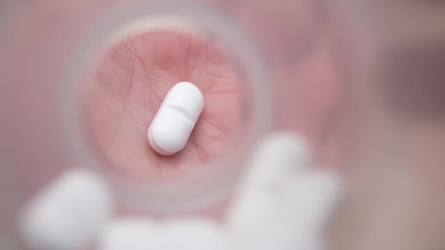 Point of view from inside a pill bottle as a white tablet falls from a person's hand. Slow-motion macro shot for medical concepts