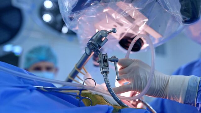 Hand of a doctor in latex glove holds a tool with a tube. Low angle view. Process of modern neurosurgical operation.