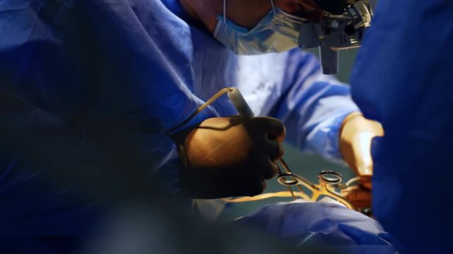 Male surgeon in blue robe and brown latex gloves uses medical tools. Doctor wearing surgical loupes works at neurosurgery.