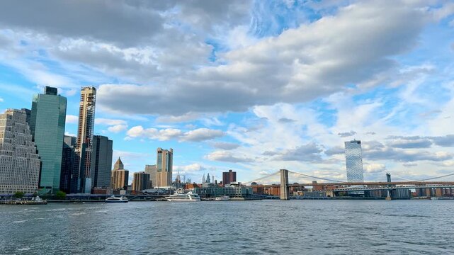 View on the bridges and stunning Manhattan from the riverscape. White fluffy clouds in the blue sky over the scenery.