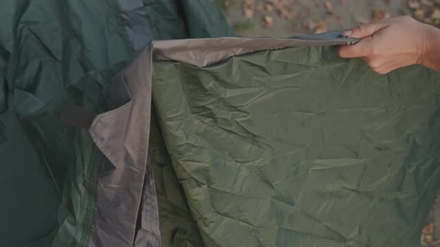 Hands threading tent pole green fabric careful daytime closeup showing nylon sleeve seam connector grip camper assembles tent at leafy campsite stepbystep setup tutorial practical camping gear demo