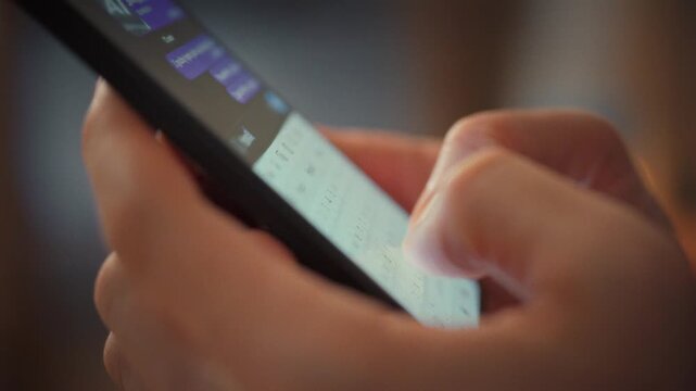 A man's hands tap a smartphone keyboard, drafting a messenger reply in his evening-time living room. The close-up captures swift typing, highlighting instant digital conversation in a modern home