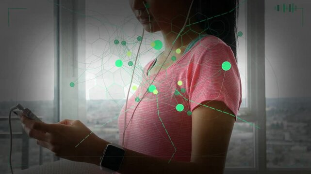 Woman tapping phone by window starting green tech overlay on torso while wearing cans for listening