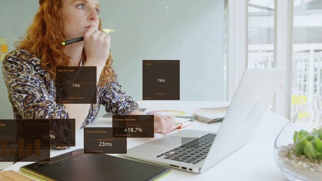 Woman working at desk by window, design panels rising, using pen and tapping laptop, checking data