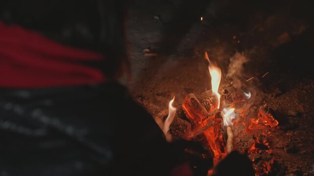 Night fire tending. Nighttime camping fire skill demonstration. Expertly tending campfire under night sky. Practicing outdoor survival by carefully maintaining fire with tools and hands