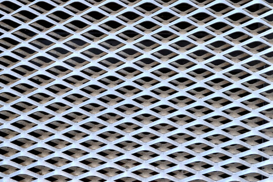 Full frame texture of silver expanded metal mesh sheet with geometric diamond pattern hole structure, industrial abstract architectural background.