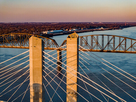 Aerial view of the Abraham Lincoln Bridge and Big Four Bridge spanning the Ohio River during a golden sunset in Louisville, Kentucky, United States.