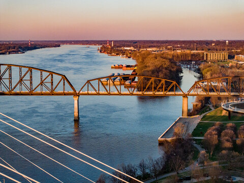 Aerial view of the Big Four Bridge spanning the Ohio River with barges docked along the shore during golden hour Louisville, Kentucky, United States.