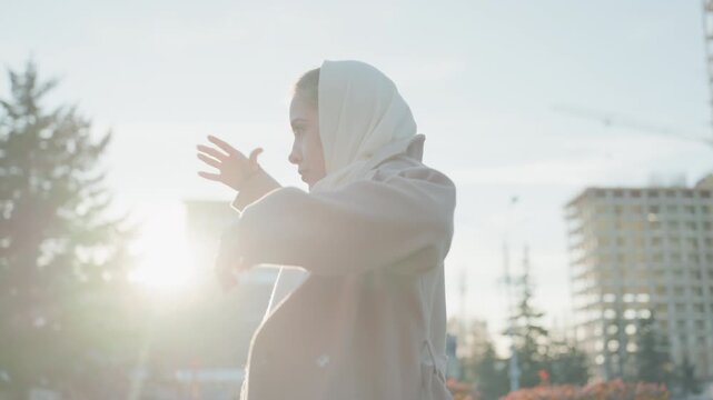 Morning lady fitting coat with city view. Early morning woman preparing outer garment with skyline backdrop. Woman in early hours adjusting her coat while overlooking cityscape at sunrise