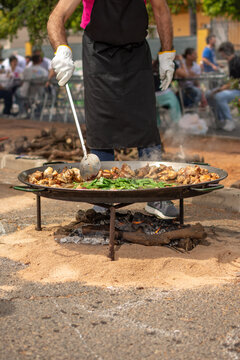 Man cooking traditional Valencian paella over wood fire outdoors