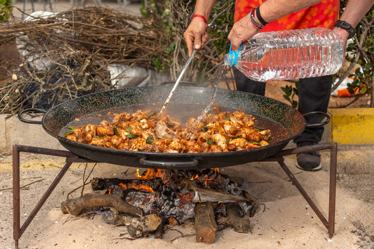 Men adding water to traditional paella over wood fire
