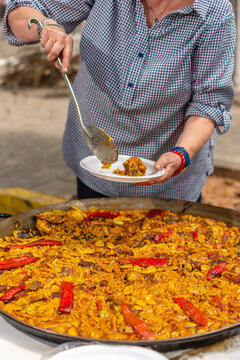 Vertical close up of senior woman serving Valencian paella