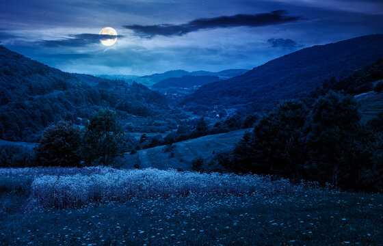 rural field on the hill at night. view in to the valley. countryside mountain landscape. full moon over alpine pasture near forested hills. inner strength to overcome fear, loneliness in darkness