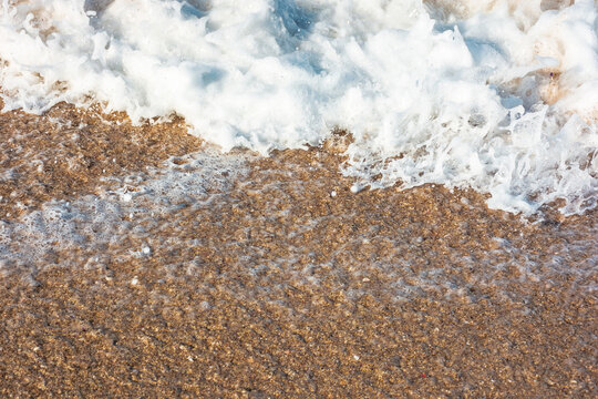 sea wave rolling foam on to the sandy beach. nature background on a sunny day. closeup texture of sea, sand, water and foam. seaside environment. tide on seashore