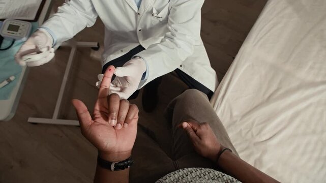 Top down view shot of doctor performing finger prick glucose test on diabetic patient from first person perspective during clinic visit