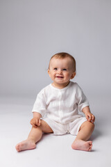 Fototapeta premium baby in a white bodysuit sits on a white background in a studio, space for text