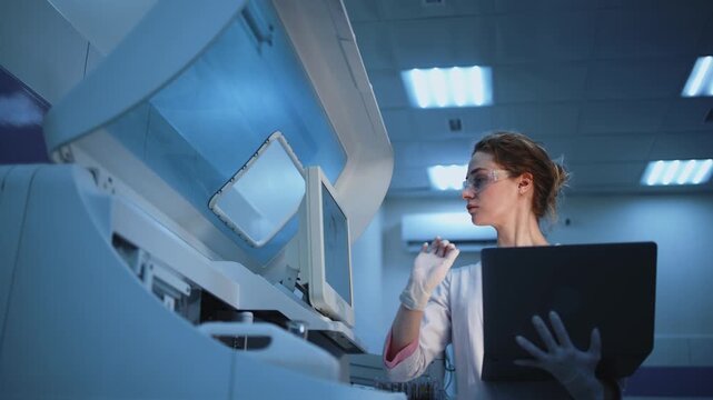 Scientist programming automated lab equipment via laptop in advanced laboratory environment. Concept laboratory innovation, virology and infectious disease diagnostics including COVID-19 coronavirus