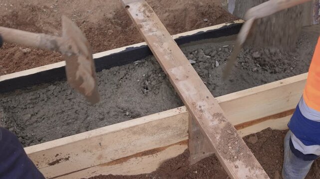Construction worker actively pouring concrete into forms. Construction worker skillfully pouring wet concrete into formwork amid surrounding earth and safety gear