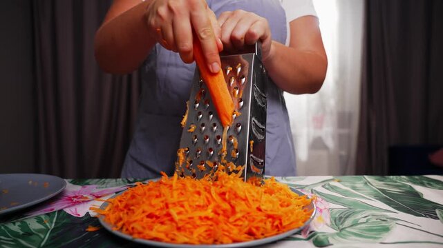 Close up of female hands grating fresh carrot with kitchen grater during homemade cooking process with healthy vegetables for delicious meal preparation. High quality 4k footage