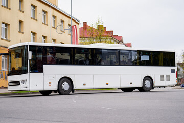 Obraz premium Large white passenger vehicle for tourism and intercity travel navigating a European town street showcasing automotive logistics and mass transport system efficiency