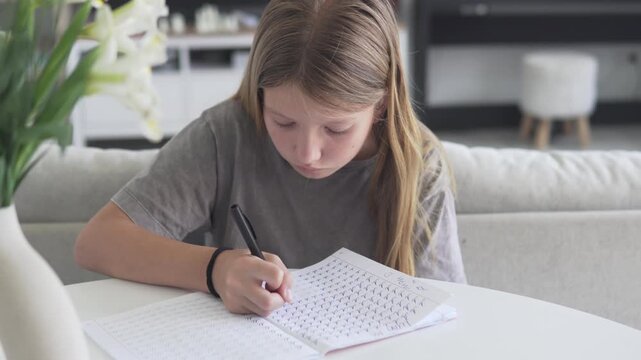 Young schoolgirl practicing handwriting in a workbook at home, focused on writing letters at a bright table. Authentic KnowledgeForAll education video showing home learning, schoolwork, early literacy