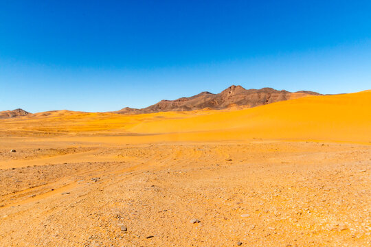 The Sahara Desert. A serir-type desert.  Flat, gravelly  desert terrain. The Tadrad Rouge mountains in the background. Algeria, Africa