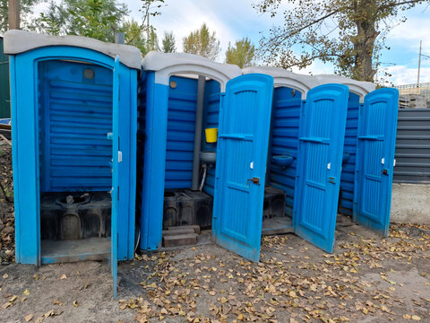 Blue plastic toilet cabins with open doors near construction site, for workers