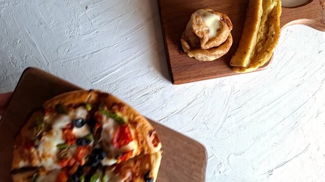 Serving Small Homemade Veggie Pan-Style Pizza on Rustic Wooden Cutting Board with Cinnamon Roll and Slice of Breadstick on Textured White Surface