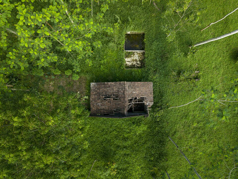 Aerial view of an abandoned house with a damaged tiled roof surrounded by dense green vegetation and trees in Cangkringan, Special Region of Yogyakarta, Indonesia.