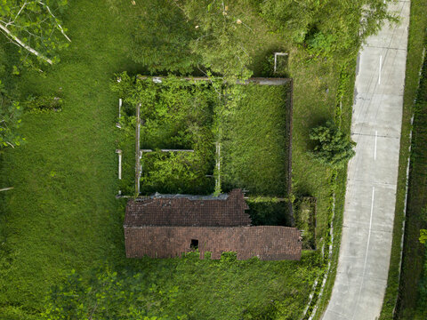 Aerial view of Houses Damaged by Mount Merapi Eruption showing a ruined structure with a broken roof and overgrown vegetation in Cangkringan, Special Region of Yogyakarta, Indonesia.