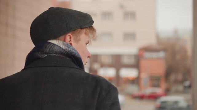 Creator walking urban corridor, alert glance back at street, scout photographer vibe, beanie and scarf, concrete pillars, overcast day, candid composition, low contrast tones, searching for shot