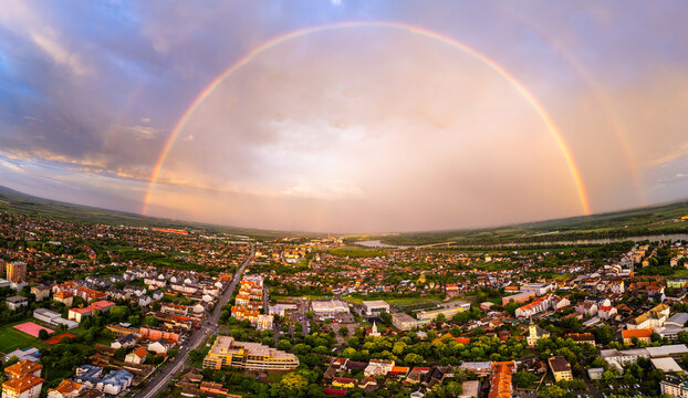Aerial view of a vibrant double rainbow arching over the urban landscape and residential rooftops at sunset Sremska Mitrovica, Serbia.