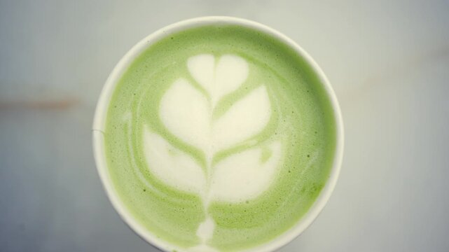 Top down view of a green matcha latte with detailed leaf shaped latte art made from steamed milk