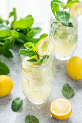 Fototapeta premium A summer drink with lemon, mint, and ice in a two glasses on a concrete background.