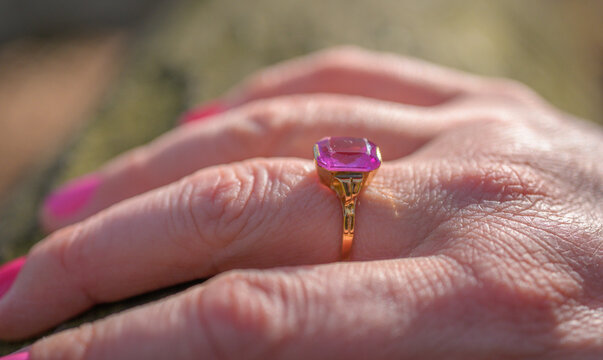 Side profile of pink gemstone ring on finger highlighting gold band and texture.