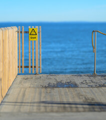 Fototapeta premium End of pier with safety sign warning of diving into shallow water against calm sea backdrop.