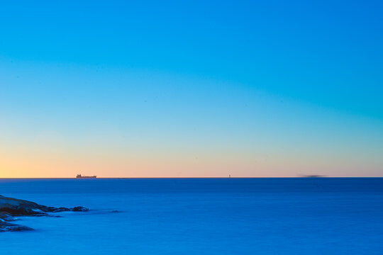 Minimal calm seascape with distant ship and soft pastel sky tones.