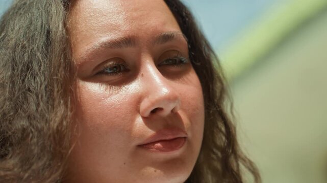 Closeup woman speaking near shore, seaside friend delivering candid monologue on island promenade, soft sunlight on face, expressive lips and eyes, casual jewelry, warm conversational mood