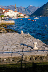Fototapeta premium Visitors enjoy the serene view of Perast by the Adriatic Sea, where boats rest peacefully against a backdrop of mountains