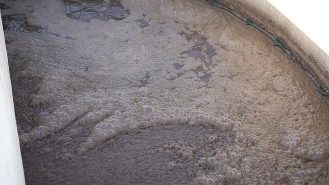 Close-up of churning, bubbling activated sludge and foam in a wastewater treatment aeration tank. Essential B-roll illustrating water pollution, biological sewage treatment, and ESG infrastructure.