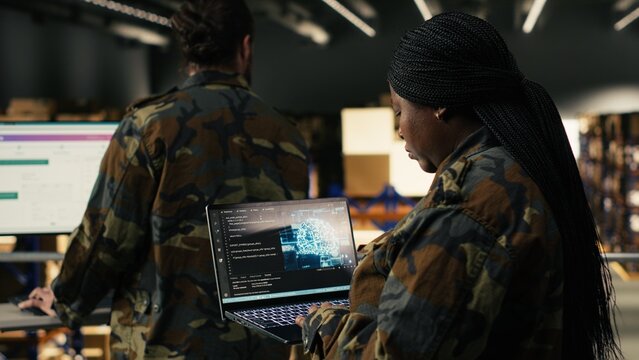 Black soldier leveraging artificial intelligence and cloud computing, warehouse management for defense logistics. Woman reviewing AI software interface with neural networks for security.