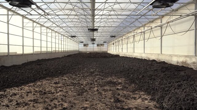 Cinematic tilt-down shot inside a solar sludge drying greenhouse revealing a massive bed of biosolids. Essential B-roll for projects on ESG, the circular economy, and sustainable waste management.