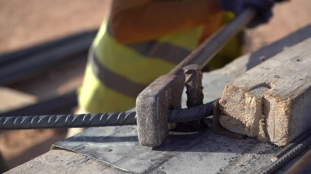 Extreme close-up of a heavy-duty manual lever tool bending steel rebar at a sunlit construction site. Highlighting rugged ironwork, this cinematic B-roll is essential for civil engineering.