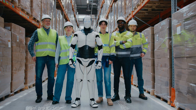 Warehouse staff standing proudly with humanoid robot in storage aisle. Wearing protective gear. Collaboration between humans and AI in logistics environment. Modern distribution center.