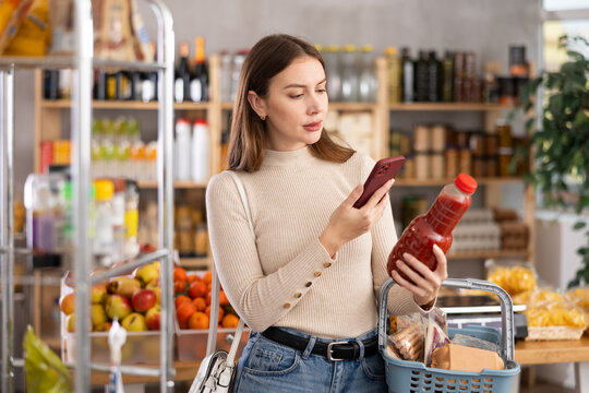 Young woman buyer scanning qr code for fresh tomato juice in bottle in grocery store
