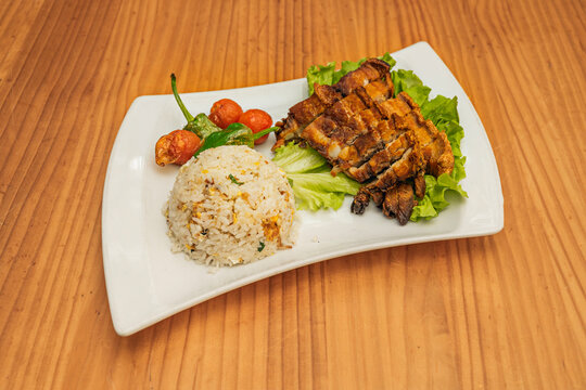A Filipino recipe of pieces of fried pork cracklings with moro rice on a white porcelain tray on pine wood.