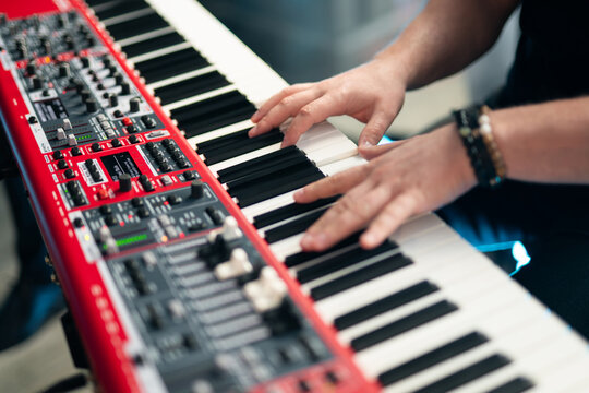 Close-up of musician's hands playing a red professional electronic keyboard synthesizer