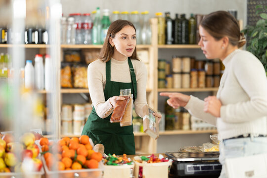 Woman salesman in an apron offers a customer soft nougat, turrons and natural sweets in a supermarket. Buying and choosing delicious desserts for the family.