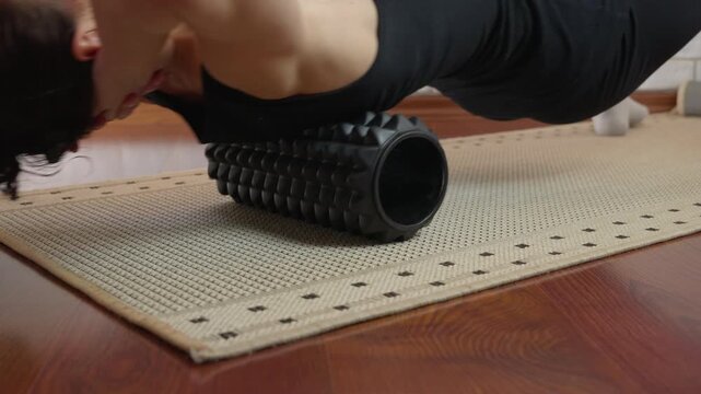 Woman massaging neck and upper back with foam roller. Athletic woman in black sportswear performing a myofascial release exercise on her upper back and neck, using a black foam roller on a mat